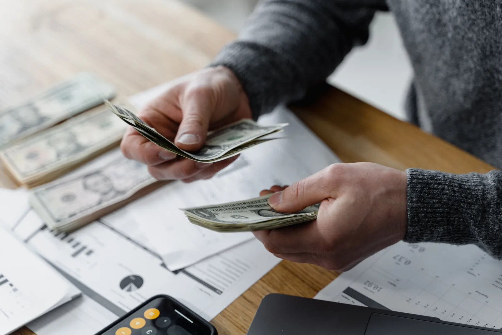 Person counting dollar bills on a desk with financial documents and a calculator in the background. Public accounting salaries at US firms compared by city and career stage