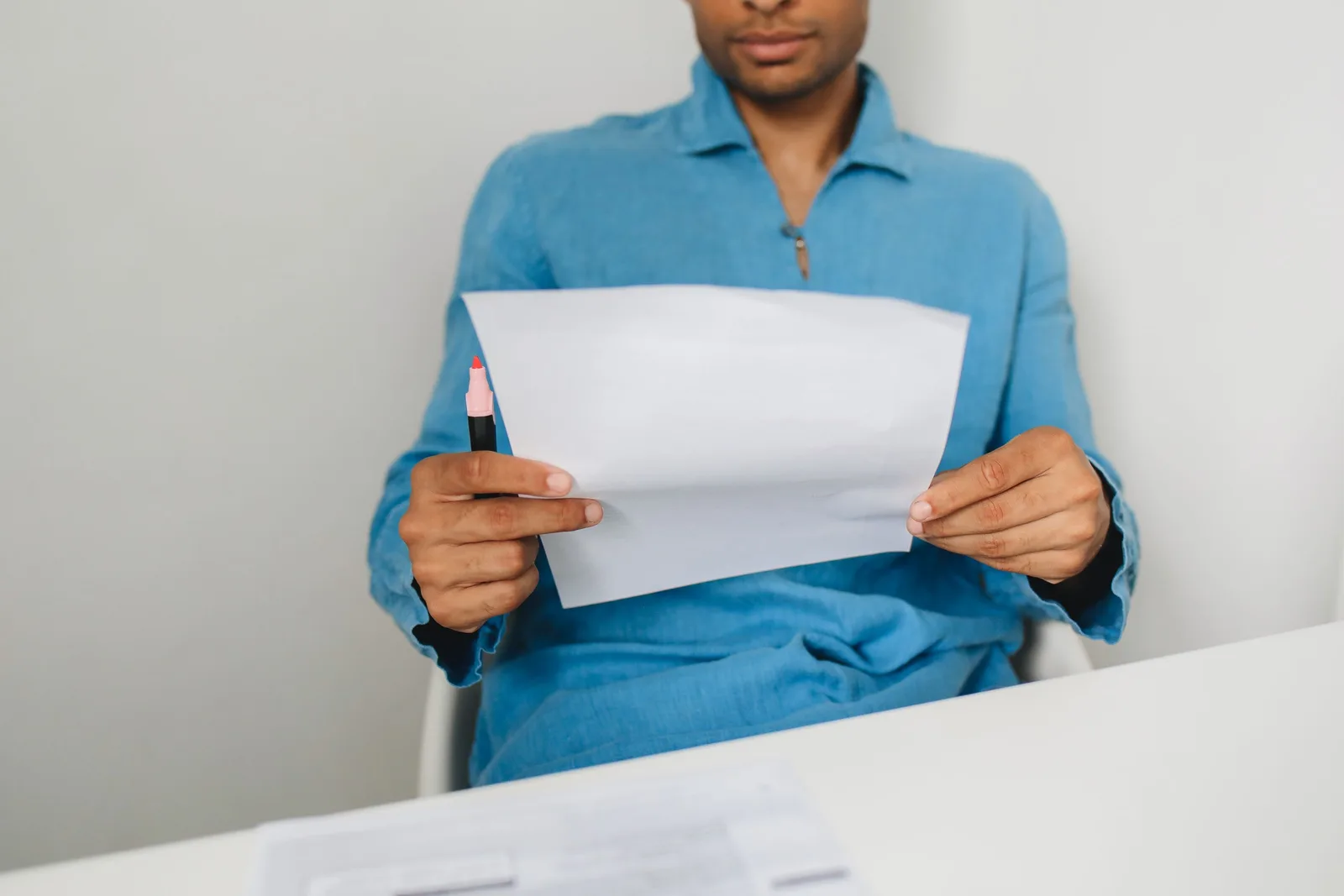 Close-up of a man holding and examining a paper with a pen indoors. How to Read Base Salary, Bonus and Equity in an Offer