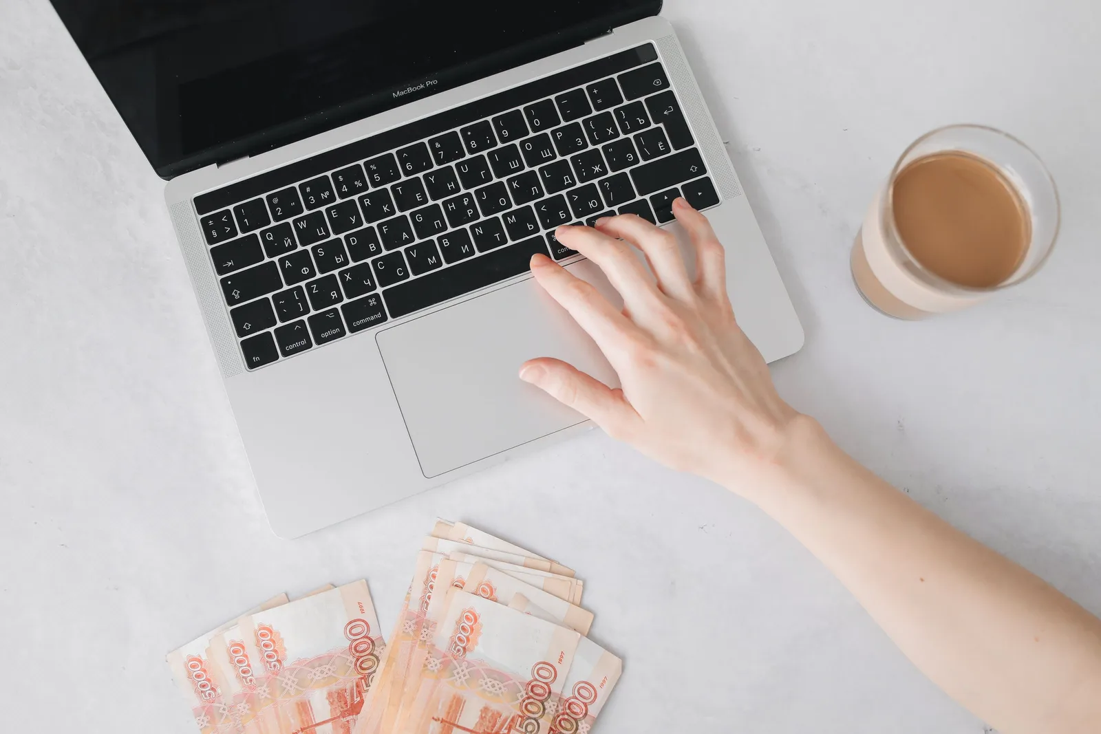 Close-up of a hand on laptop keyboard with cash and coffee on table. Salaries and advancement courses: what to check