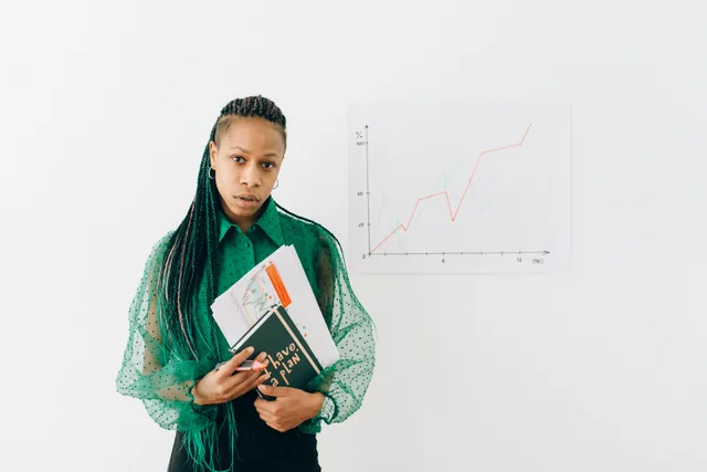 A professional woman stands confidently with documents and a graph, symbolizing business analysis. Employers that are good on pay tend to share four specific traits