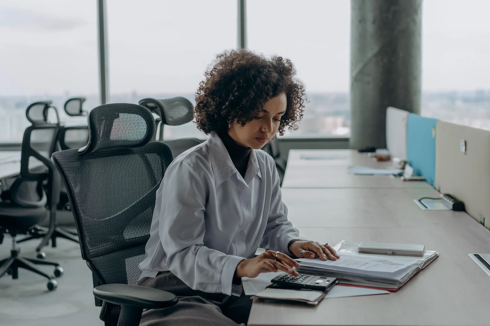 A professional woman with curly hair calculating documents in a modern office setting. CPA Canada salary guide: illustrative pay and paths