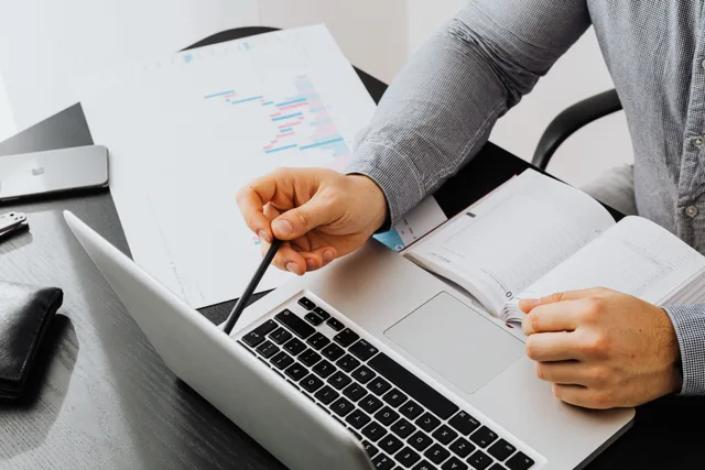 Professional using laptop and reviewing documents at office desk for data analysis. HR business partner salaries vary by industry: what drives the spread
