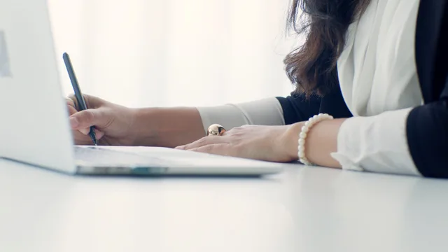A professional woman writing at her desk in an office setting, showcasing elegance and focus. The salary conversation in interviews: who holds which lever and when
