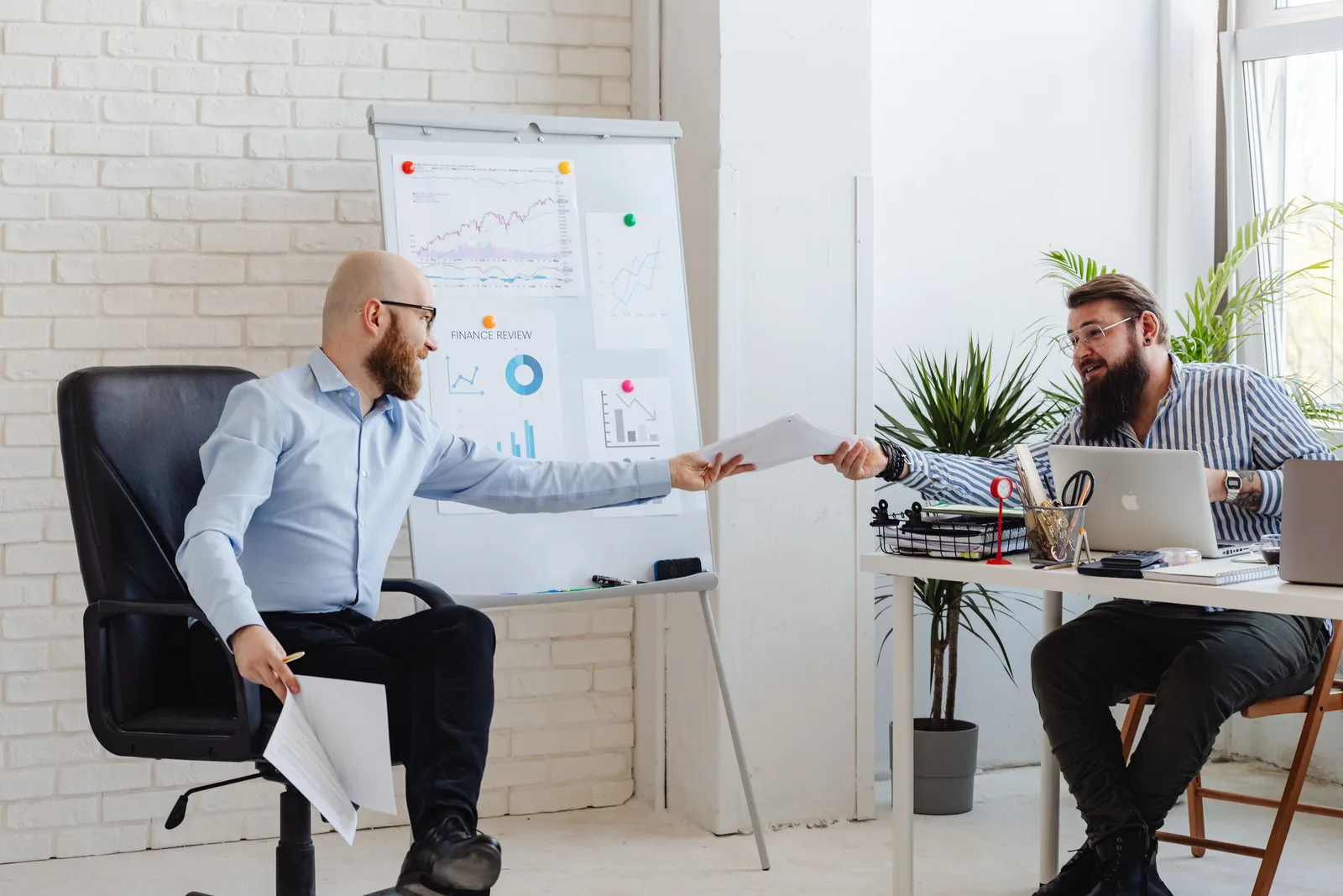 Two business professionals exchanging documents in a modern office setting with charts and graphs. Salary raises compared: merit money, market adjustment, and promotion